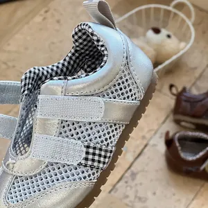 Close-up of silver mesh baby walking shoes with checkered lining and Velcro straps.