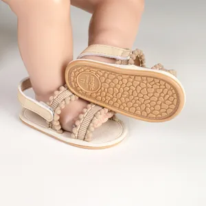 Nahaufnahme von atmungsaktiven Babysandalen mit Pompons und rutschfesten Gummisohlen.