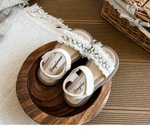 Detail of girl's white summer sandals featuring delicate lace ruffles and pearl flower accents