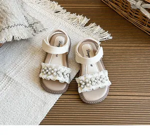 Detail of white girl sandals with pearl flowers and lace ruffles on warm background.