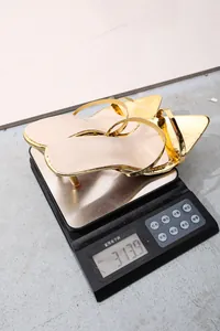 Detailed view of gold pointed-toe high-heeled slippers being weighed at 313.9g on a scale.