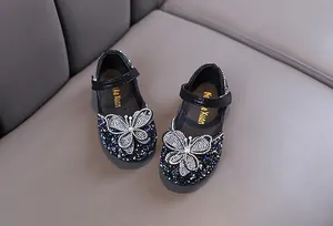 Gros plan sur les chaussures de princesse à strass noirs pour filles avec papillon en cristal.
