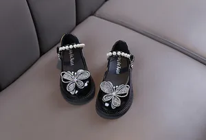 Primer plano de zapatos Mary Jane negros para niña con mariposa de pedrería y tira de perlas.