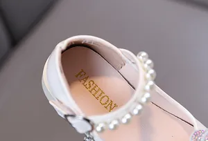 Detalle de zapatos de princesa blancos para niñas con correa de perlas y toques de brillo.