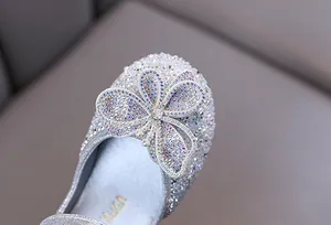 Gros plan de chaussures princesse argentées pour filles avec détail papillon en strass.