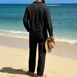 Vista detallada trasera de un hombre con camisa y pantalón de lino negro en la playa
