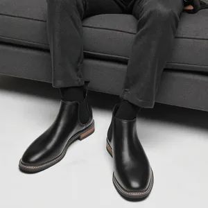 Gros plan de bottines Chelsea en cuir noir pour homme portées sur un canapé