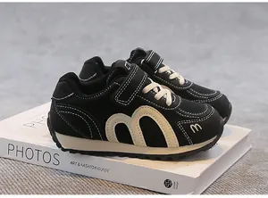 Close-up of breathable black kids' sneakers with beige M logo and mesh texture.
