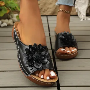 Primer plano de sandalias de cuña negras para mujer con una gran flor decorativa.