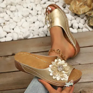 Vista detallada de sandalias de cuña doradas para mujer con aplique de flor.