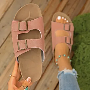 Close-up of pink suede double buckle slide sandals for women on a rustic wooden deck