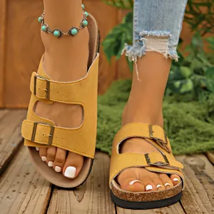 Detailed view of yellow suede double-buckle sandals worn by a model in a rustic outdoor setting