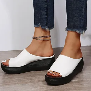Detail view of white wedge peep-toe sandals with thick black soles on a model's feet.