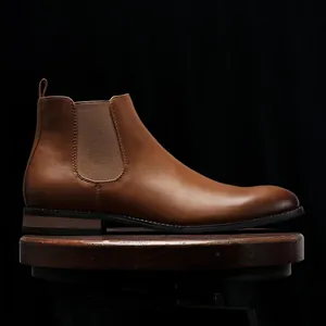 Side view detail of a classic brown leather Chelsea boot displayed on a dark wooden stool