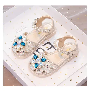 Girls' beige princess sandals featuring a rhinestone flower and pearl-studded ankle straps.