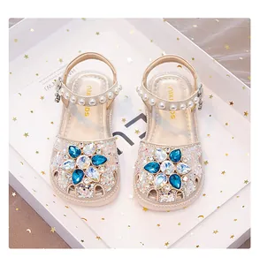 Detail of girls' princess sandals with blue crystal flower and pearl strap in glitter beige.