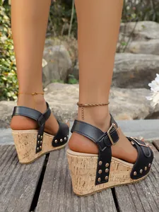 Close-up side view of black wedge sandals featuring gold rivet decor and cork texture heels