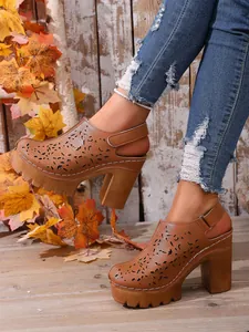 Mules platform marroni con motivi traforati e tacco largo in un ambiente autunnale.