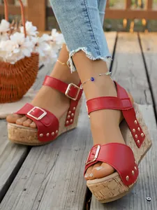 Close-up of red wedge sandals with buckle straps and rivet details on a wooden deck