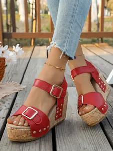 Detailed view of red wedge sandals with buckle straps and rivet accents on a wooden deck