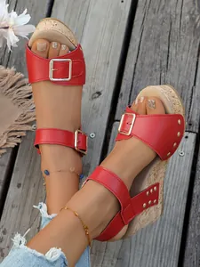 Detailed close-up of red wedge sandals featuring stylish buckles and metallic rivet accents