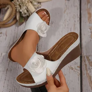 Detail von weißen Keilsandaletten mit einer stilvollen 3D-Rose und Kontrastnähten.