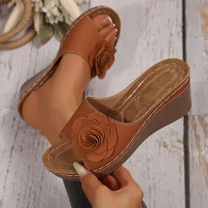Detail der braunen Keilsandaletten mit großer Blumenverzierung und Kontrastnähten.