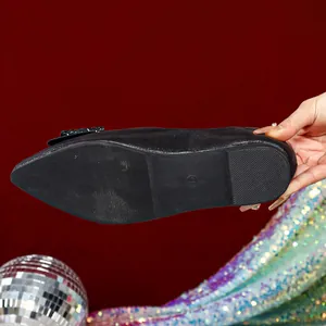Close-up of black pointed-toe flat shoe with bow and shimmer detail on red background