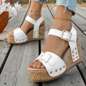 Elegant white leather wedge sandals featuring gold buckles and rivets on a wooden deck