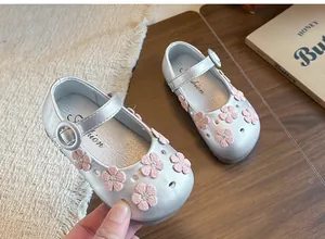 Silver girl's Mary Jane shoes with pink flower decorations on a wooden background.