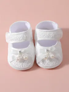 Close-up of elegant white lace baby princess shoes with faux pearl and satin bow details