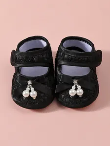 Detail view of black lace baby girl princess shoes featuring pearls and bow accents