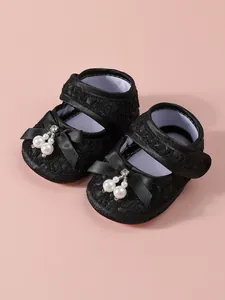 Close-up of elegant black lace baby girl princess shoes with pearl and bow details.