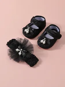 Detailansicht von schwarzen Baby-Spitzenschuhen und passendem Perlen-Stirnband-Set