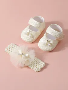Detaillierte Makroansicht der cremefarbenen Baby-Spitzenschuhe und des Stirnbandsatzes