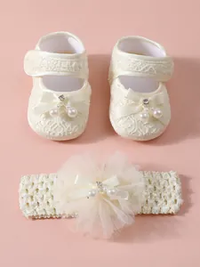 Nahaufnahme von cremefarbenen Baby-Spitzenschuhen und Blumen-Stirnband mit Perlen
