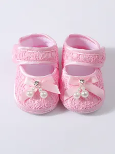 Detailed view of pink lace baby girl princess shoes with bow and pearl charms