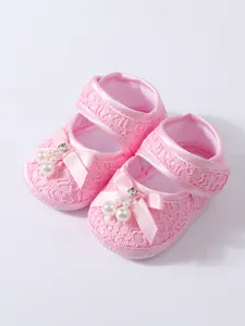 Detailed macro view of lace texture, satin bow, and pearl beads on pink baby shoes