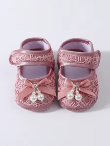 Detail view of baby girl pink lace princess shoes with elegant ribbon bows and pearls