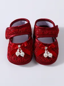 Detailed close-up view of red lace baby princess shoes decorated with elegant pearl bows