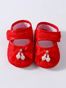 Close-up of red lace baby princess shoes featuring decorative bow and elegant pearl charms