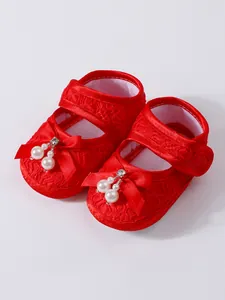 Detail of red lace baby girl shoes featuring satin bows and pearl accents