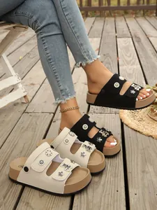 Detailansicht von schwarzen und cremefarbenen Plateausandalen mit Blumendekor auf Holzdeck.