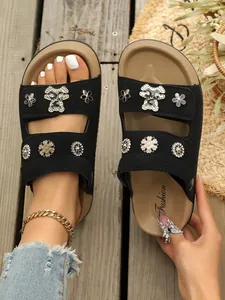 Detailansicht schwarzer Plateausandalen mit glitzernden Bären- und Blumenanhängern.