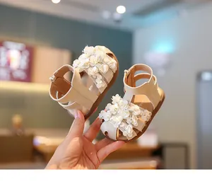 Primer plano de sandalias beige para bebé niña con flores 3D blancas y suelas blandas.
