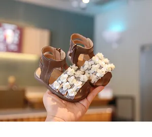 Detalle de sandalias marrones para bebé niña con elegantes decoraciones de flores blancas 3D