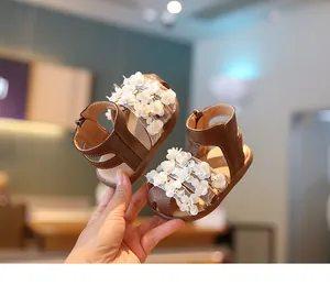 Primer plano de sandalias marrones para niñas pequeñas con apliques de flores blancas.