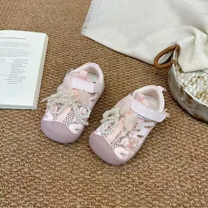 Vue rapprochée de sandales roses pour filles avec perles et rubans sur un tapis tissé marron.