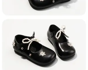 Dettaglio di scarpe in pelle nera per bambina con eleganti fiocchi di perle e strass.