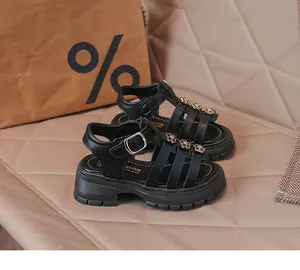 Détail de sandales romaines noires pour filles avec des accents floraux décoratifs.